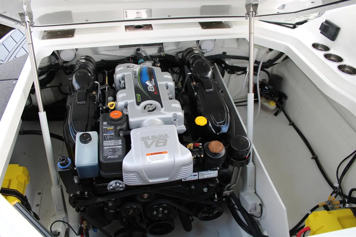 Engine room of a boat featuring a silver V8 engine, coolant reservoir, and various engine components with visible labels.